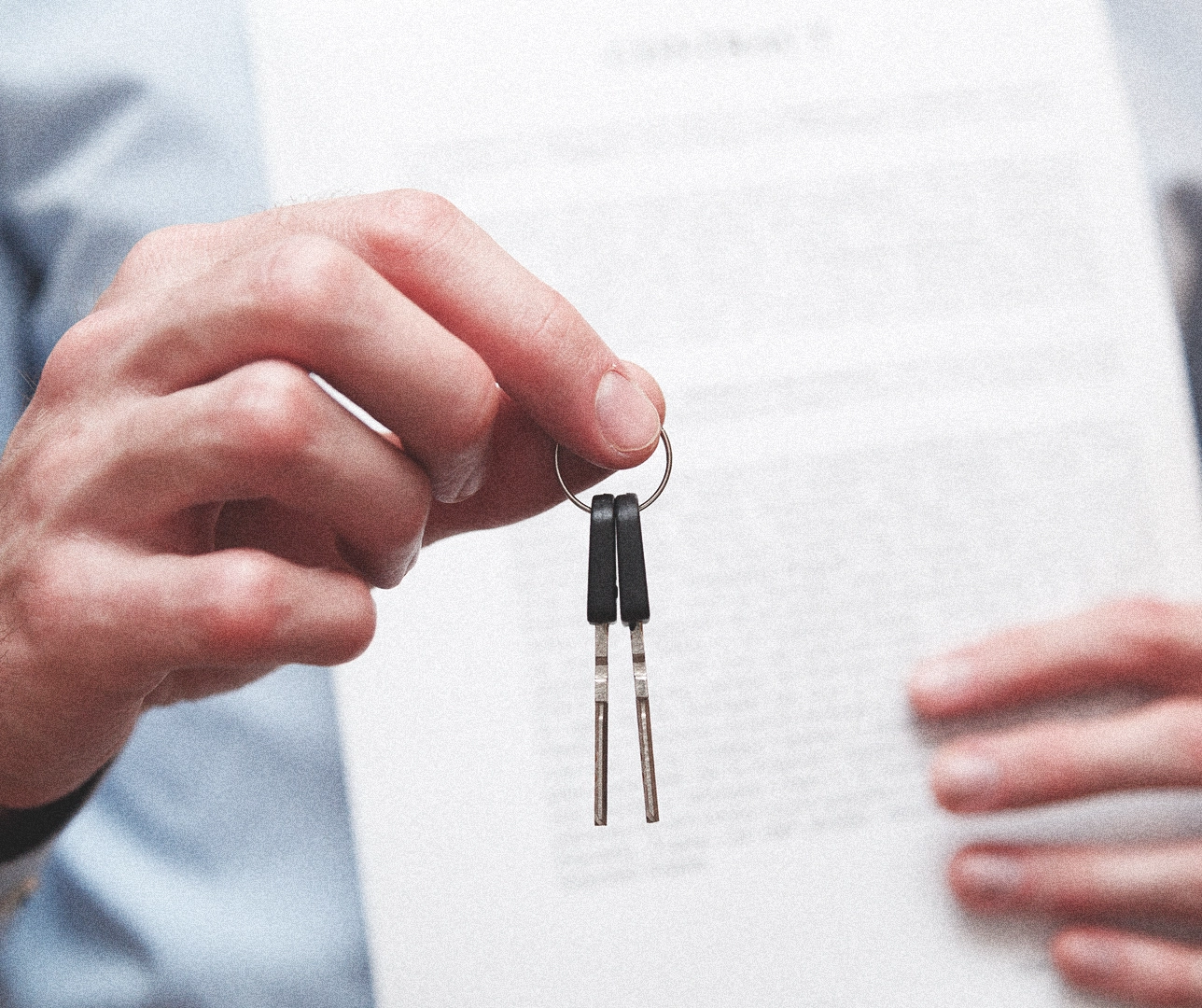 Una persona sosteniendo las llaves de una casa con un contrato de fondo.